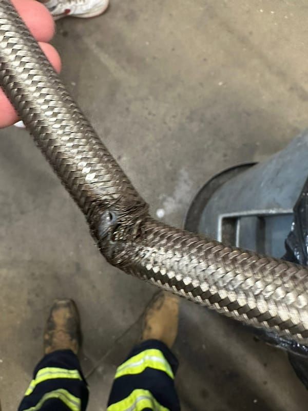 Frayed braided hose on a truck, held up by a mechanic in work boots