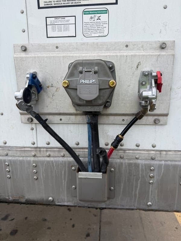 Trailer front wall with a 7-way receptacle and red and blue gladhands after a wiring repair
